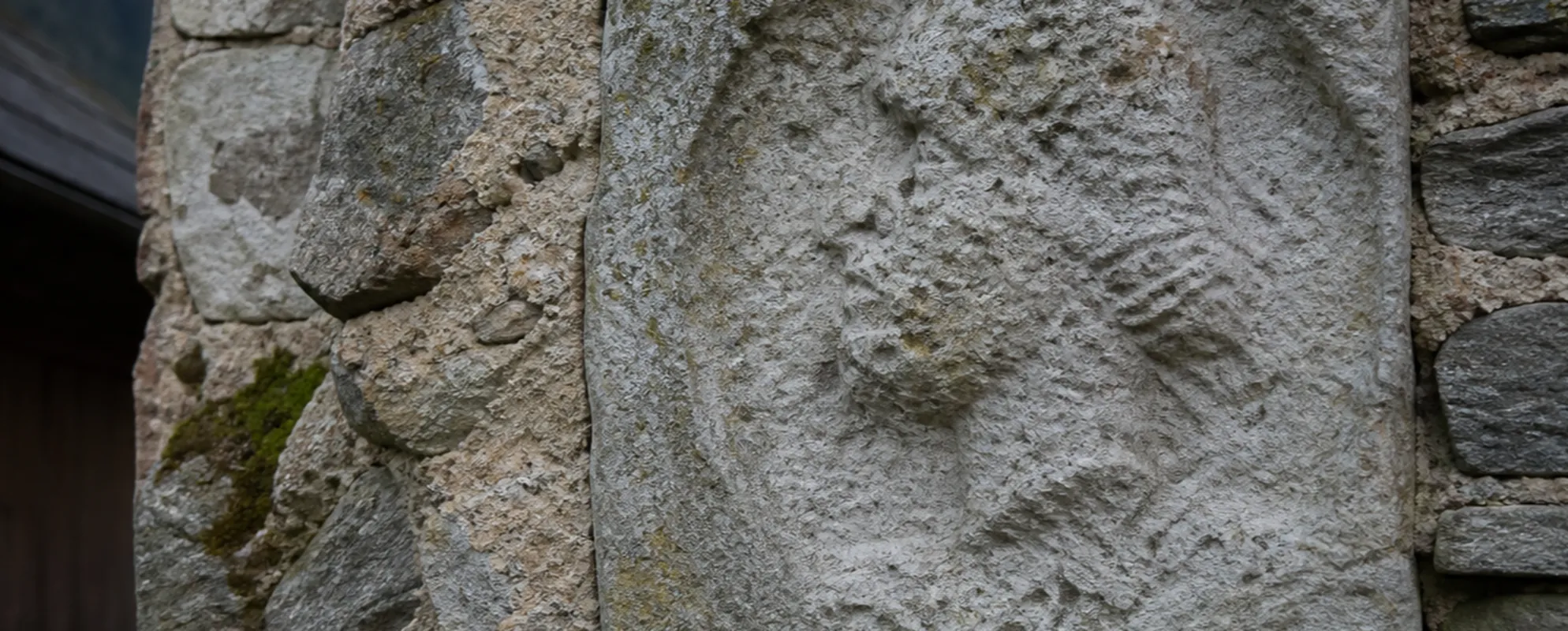 Verwitterter antiker Kalksteinquader mit abgetragenem Porträtrelief in einer Bruchsteinmauer