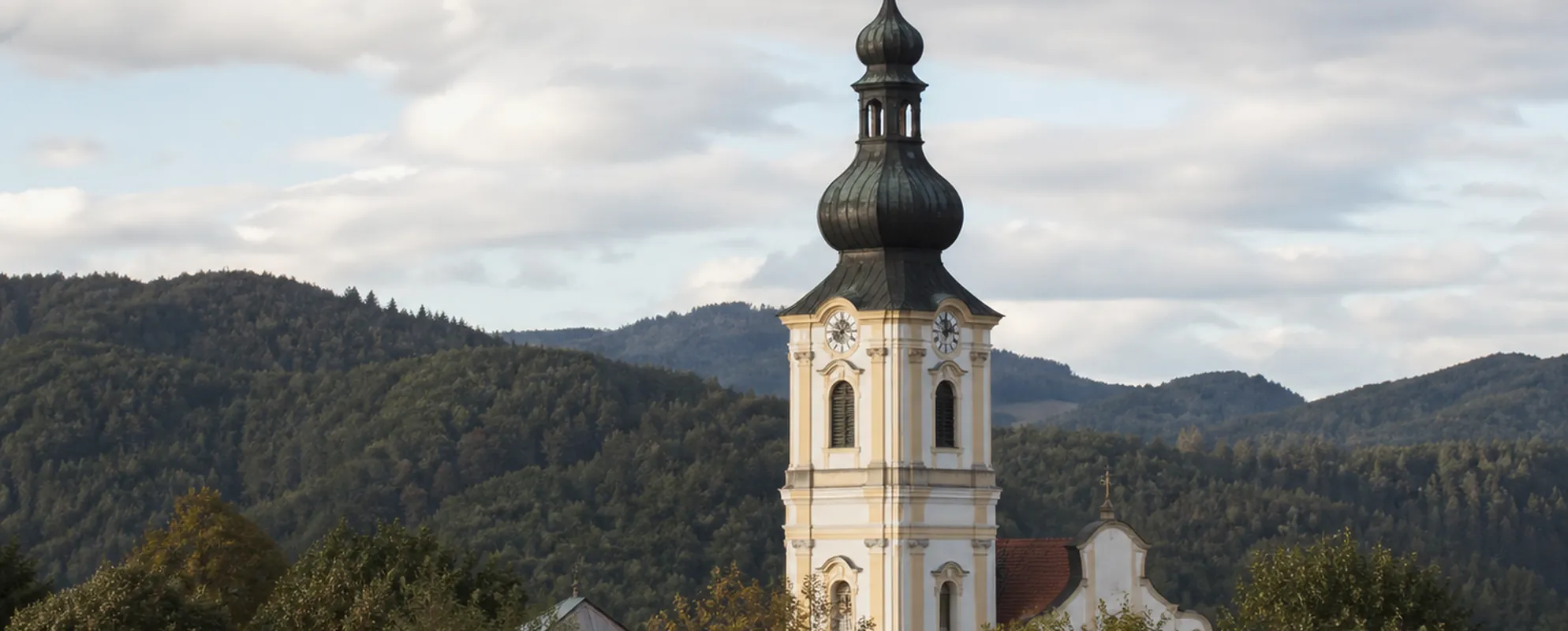 Barocker Kirchturm mit Zwiebelhaube ragt über Baumwipfel